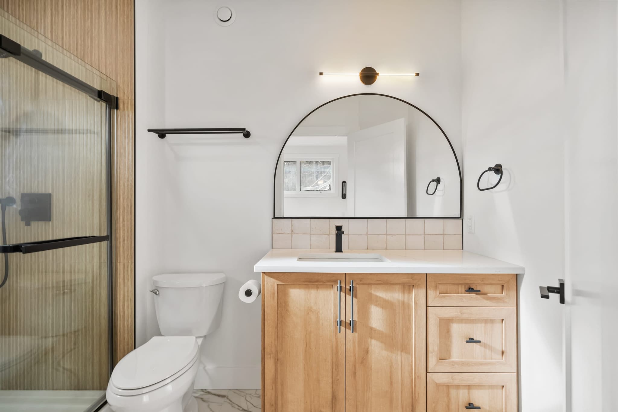 Primary ensuite with arched mirror and white-oak vanity