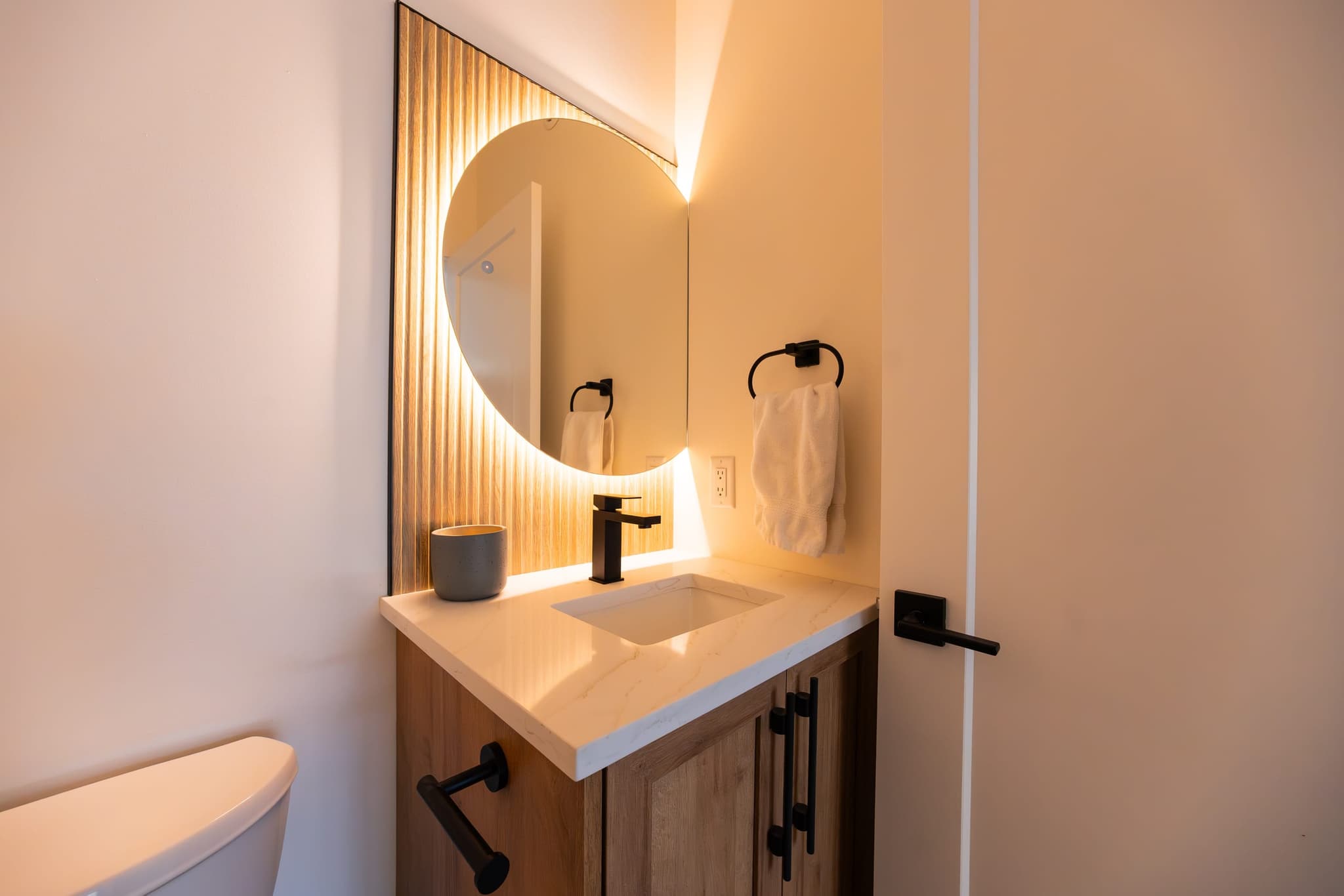 Powder room with backlit round mirror and quartz vanity